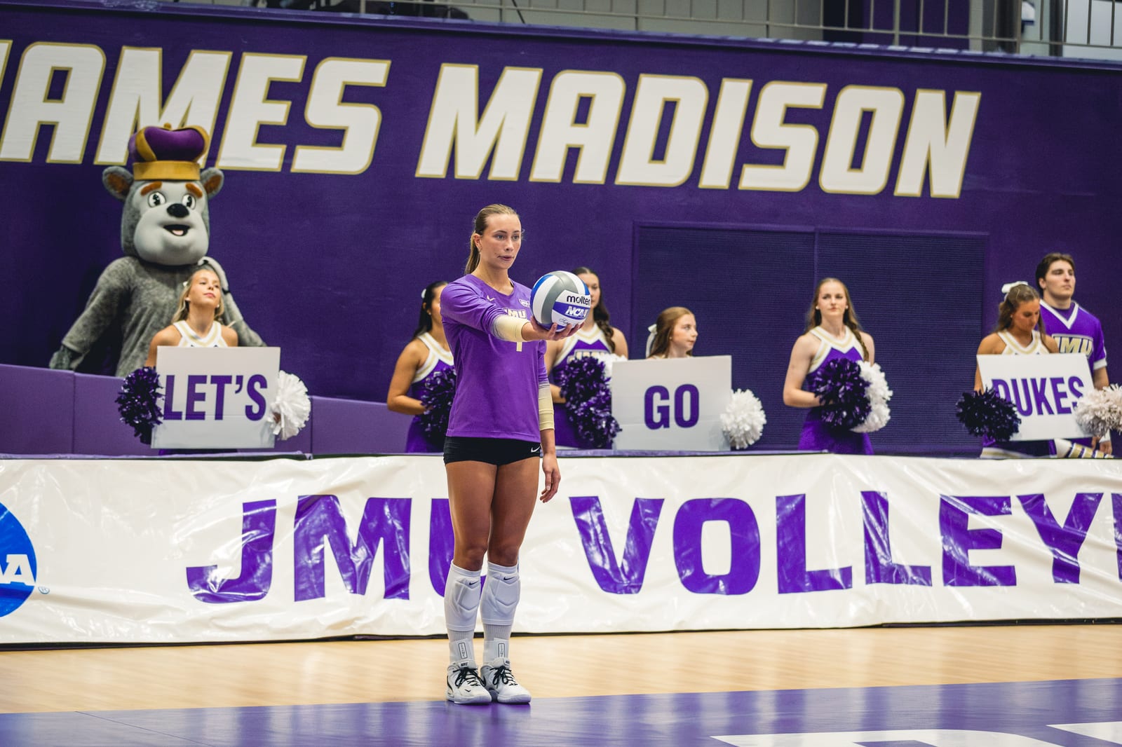 JMU volleyball player serving in front of the JMU Volleyball banner